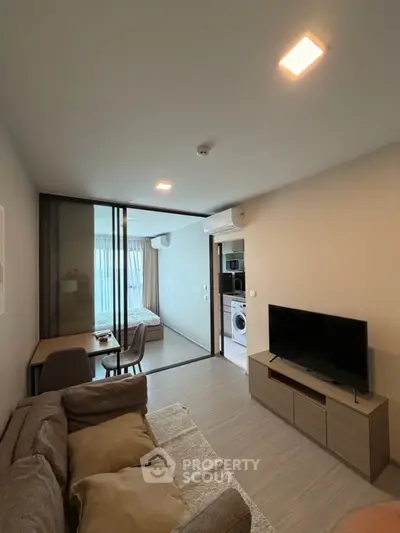 Modern living room with cozy sofa, TV, and view into bedroom and kitchen area.