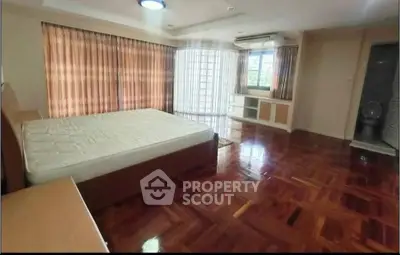 Spacious bedroom with wooden flooring and large windows for natural light.