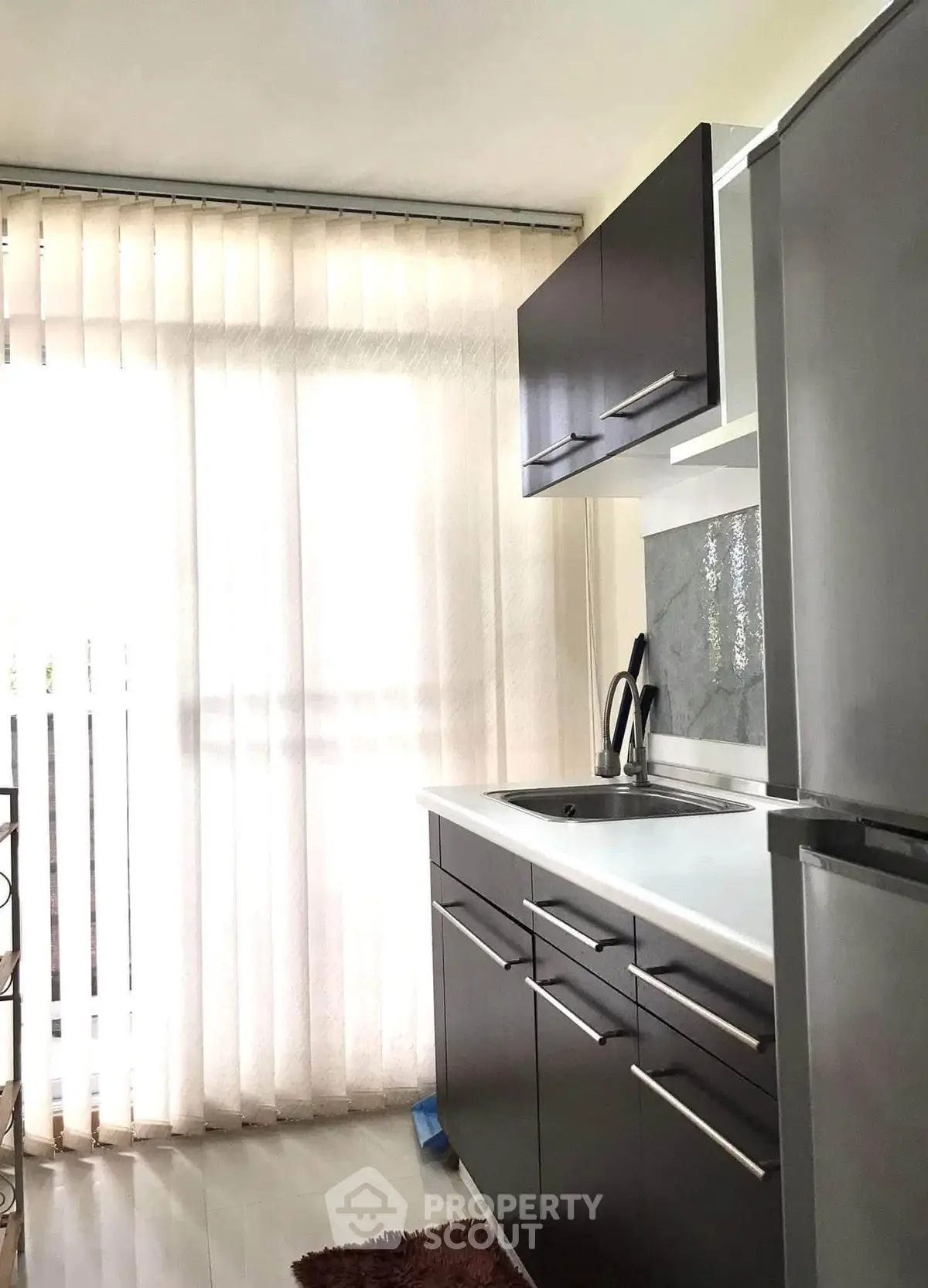 Modern kitchen with sleek cabinets and natural light through large window blinds.