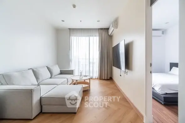 Modern living room with cozy sectional sofa and wall-mounted TV, adjacent to a bright bedroom.