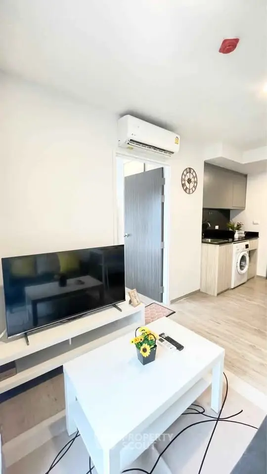 Modern living room with TV, air conditioning, and open kitchen layout featuring washing machine.