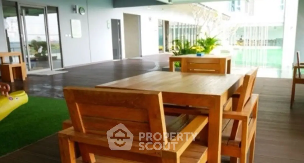 Modern outdoor seating area with wooden furniture and pool view in luxury apartment complex.