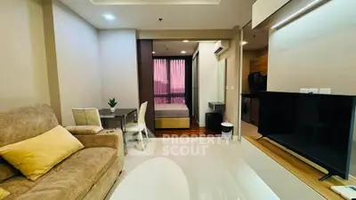Modern open-plan living room with cozy seating and sleek TV setup, leading to a stylish bedroom.