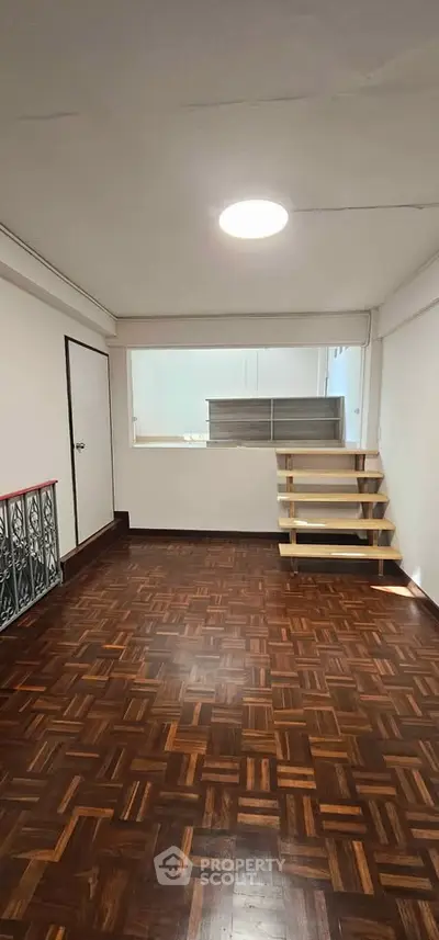 Spacious room with wooden flooring and modern staircase in a bright interior space.