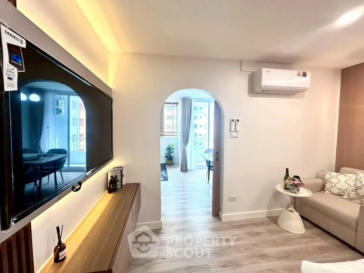 Modern living room with sleek TV and cozy seating area, leading to a bright balcony.