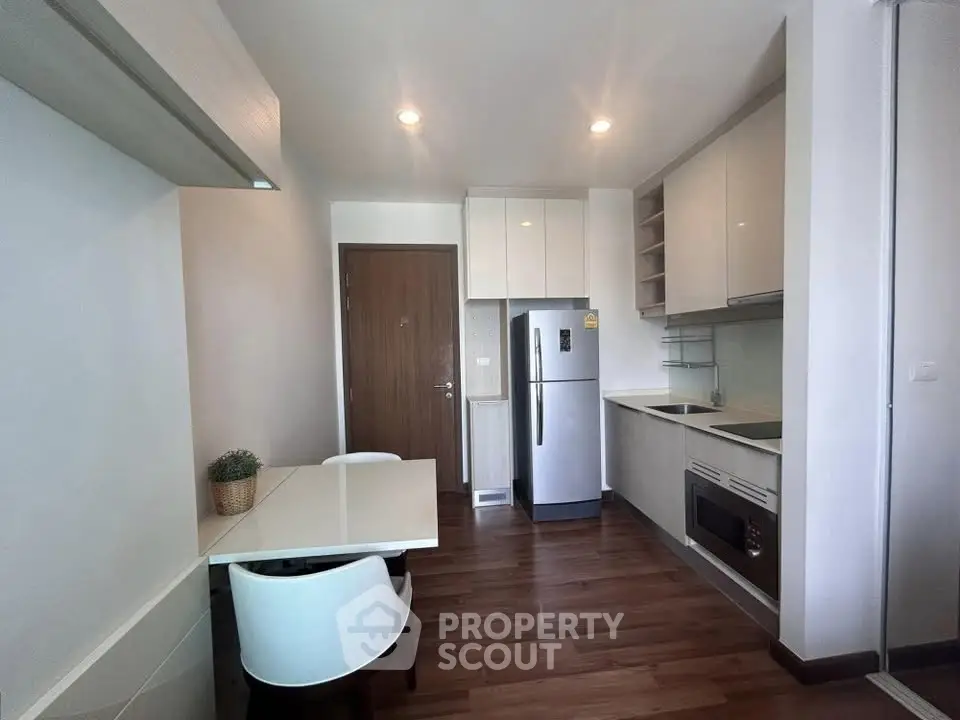 Modern kitchen with sleek cabinetry, dining area, and stainless steel appliances in a cozy apartment.
