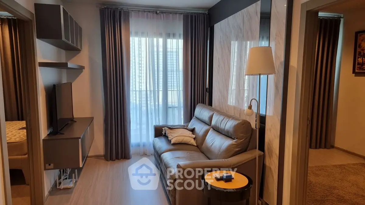 Modern living room with sleek furniture and large window offering city view.