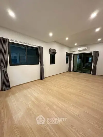 Spacious modern living room with wooden flooring and large windows for natural light.