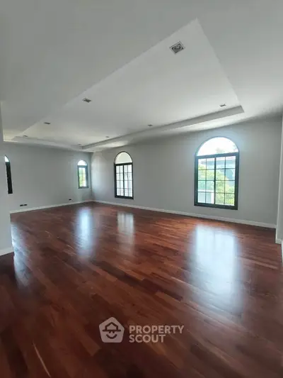 Spacious living room with elegant wooden flooring and arched windows offering natural light.
