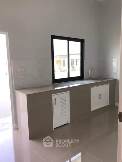 Modern kitchen with sleek countertops and large window, offering ample natural light and minimalist design.