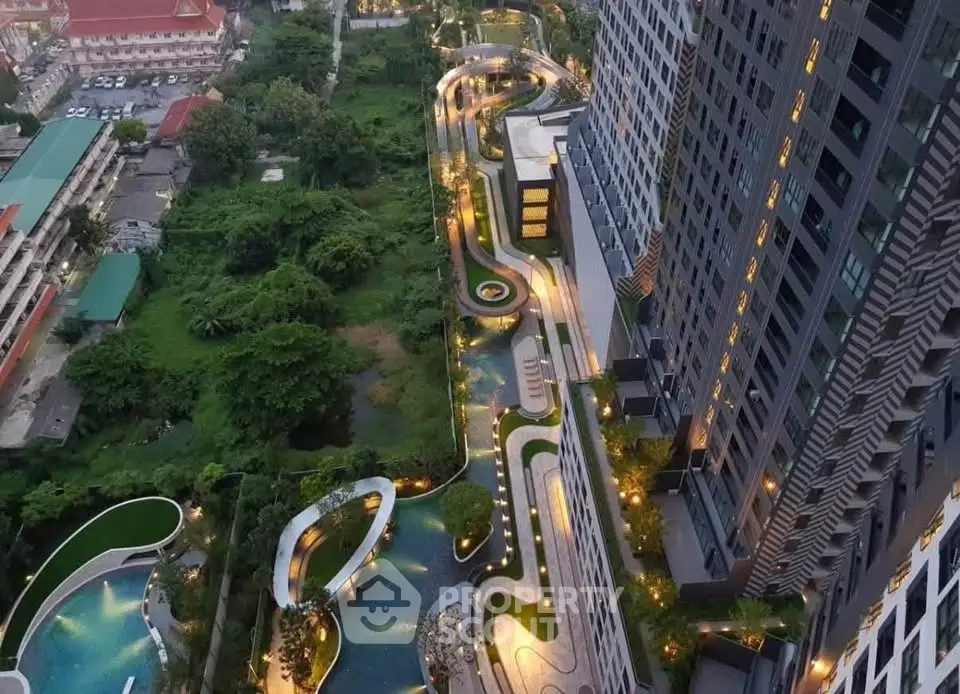 Stunning aerial view of modern high-rise building with illuminated landscaped gardens and pool area.