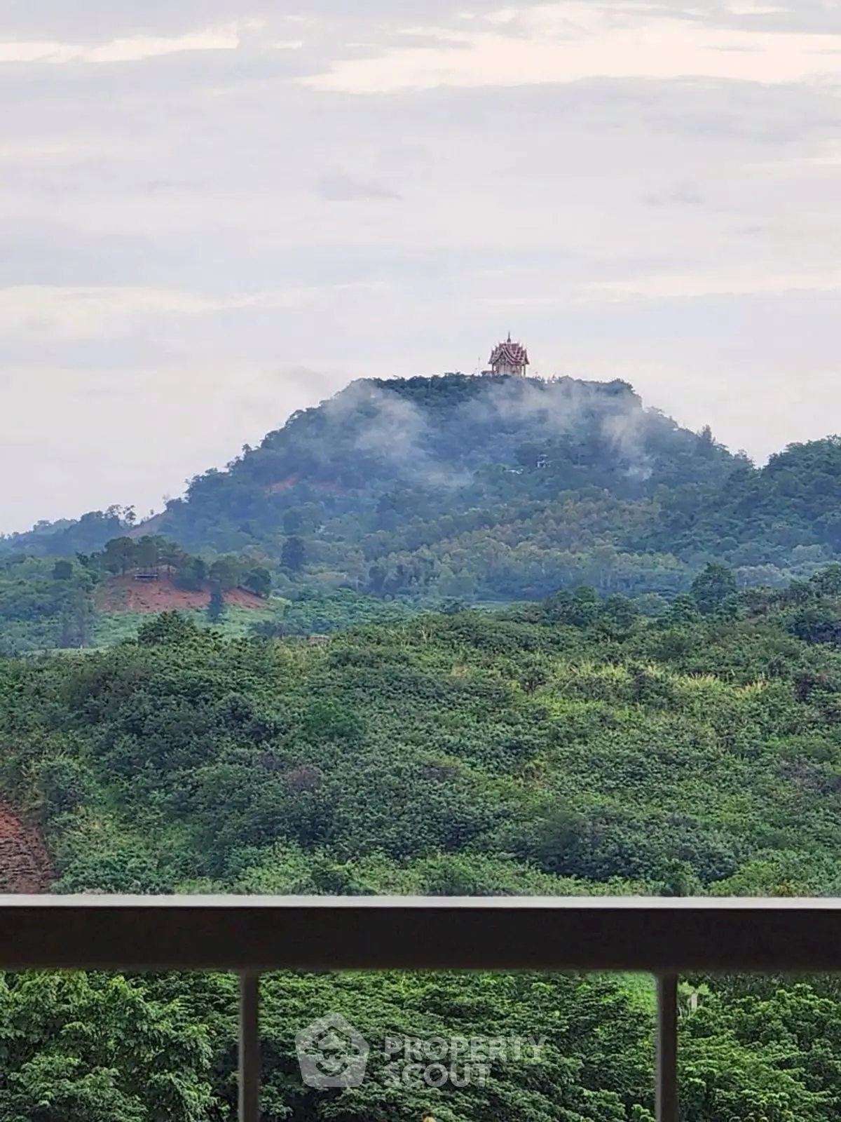 Scenic view from balcony overlooking lush green hills and distant temple