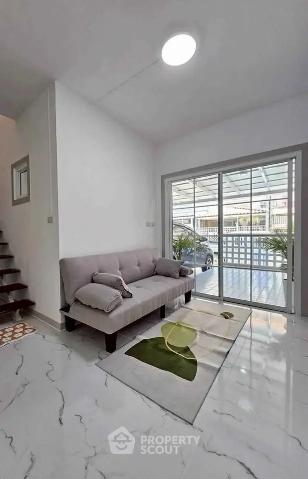 Modern living room with sleek marble flooring and cozy gray sofa, featuring large sliding glass doors to patio.
