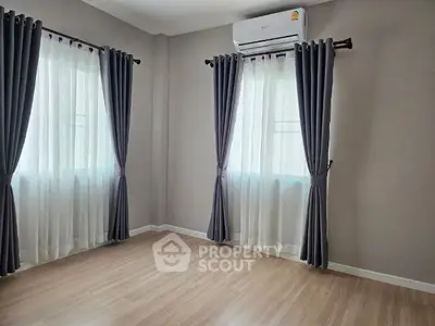 Spacious and well-lit living room with elegant dark curtains and modern air conditioning unit, featuring sleek wooden flooring.