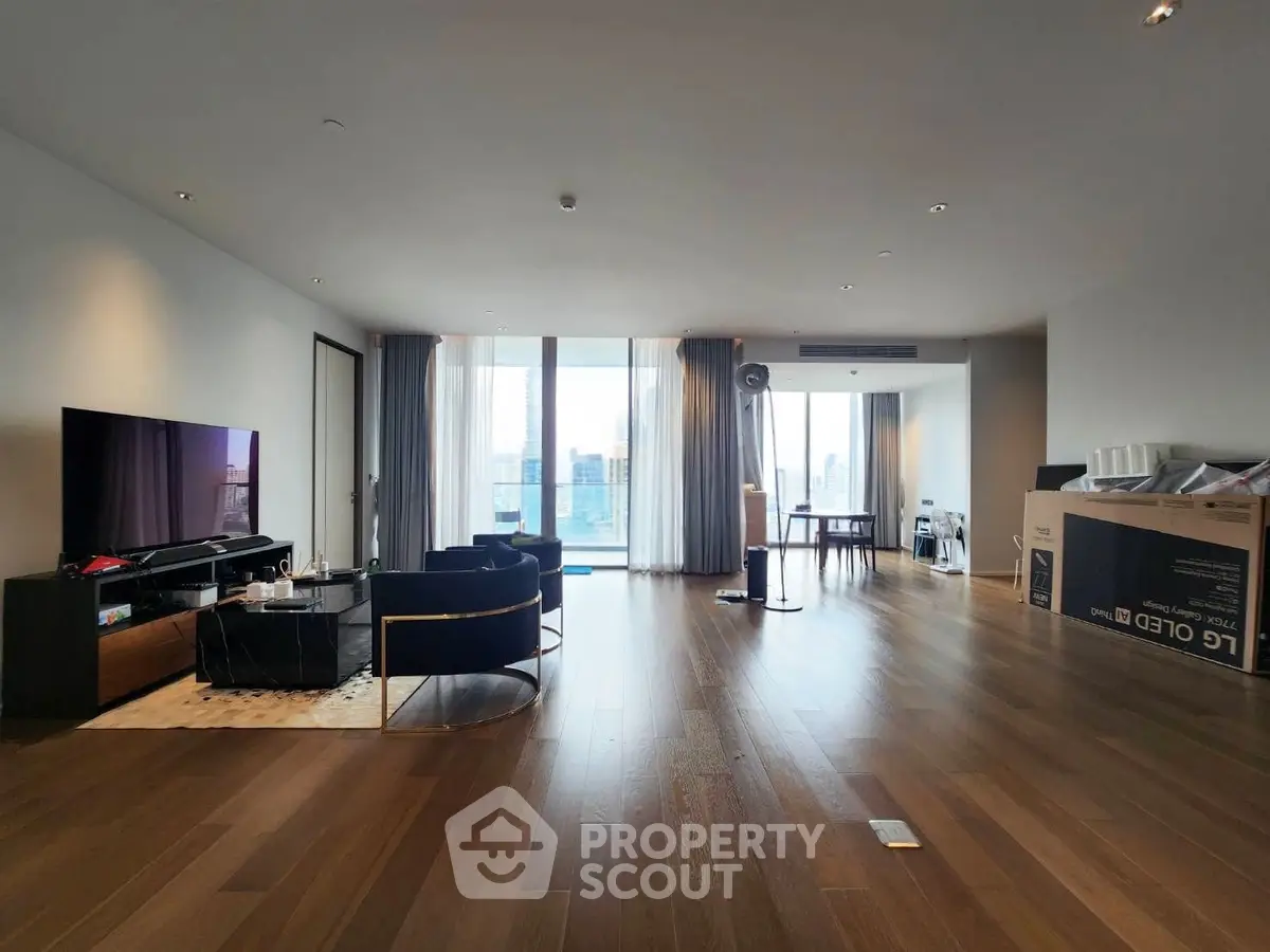 Spacious modern living room with floor-to-ceiling windows and city view, featuring elegant furniture and hardwood floors.