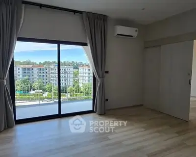 Spacious room with large window offering a scenic view of modern apartment buildings.