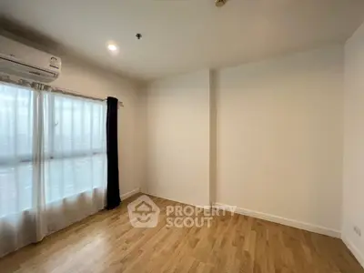 Spacious empty room with wooden flooring and large window for natural light.
