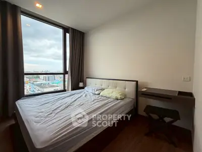 Modern bedroom with large window offering city views, featuring a comfortable bed and sleek furnishings.
