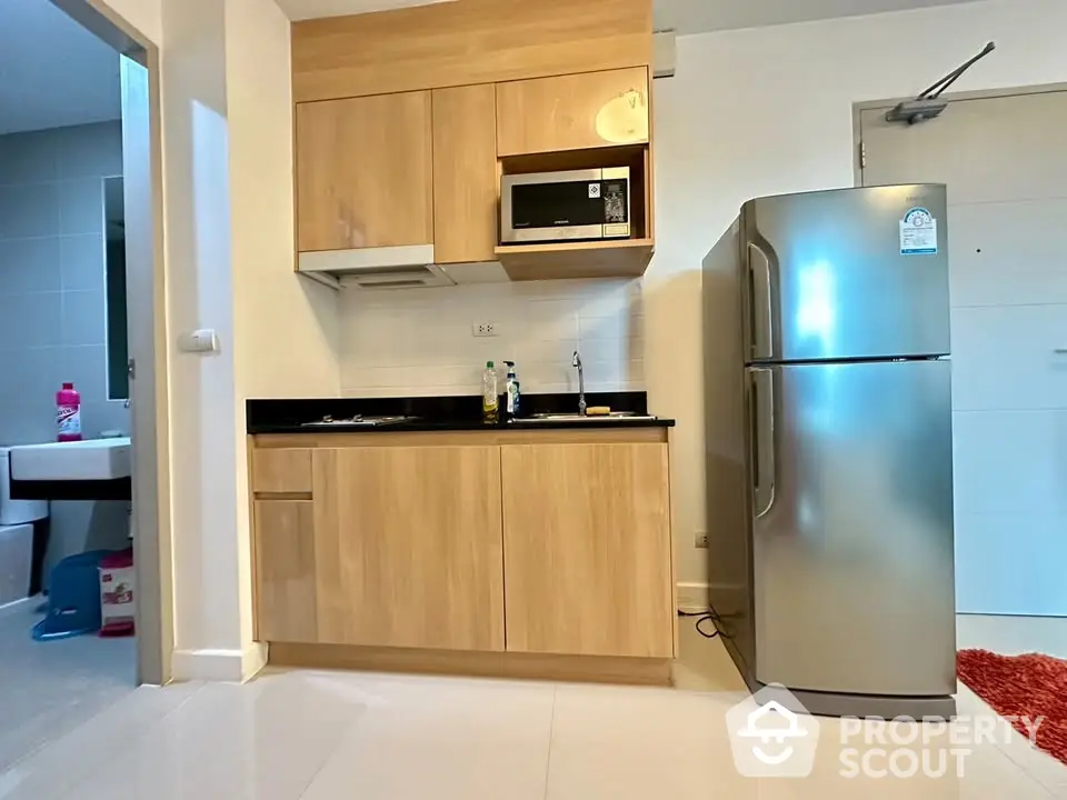 Modern compact kitchen with wooden cabinets and stainless steel fridge in a cozy apartment.