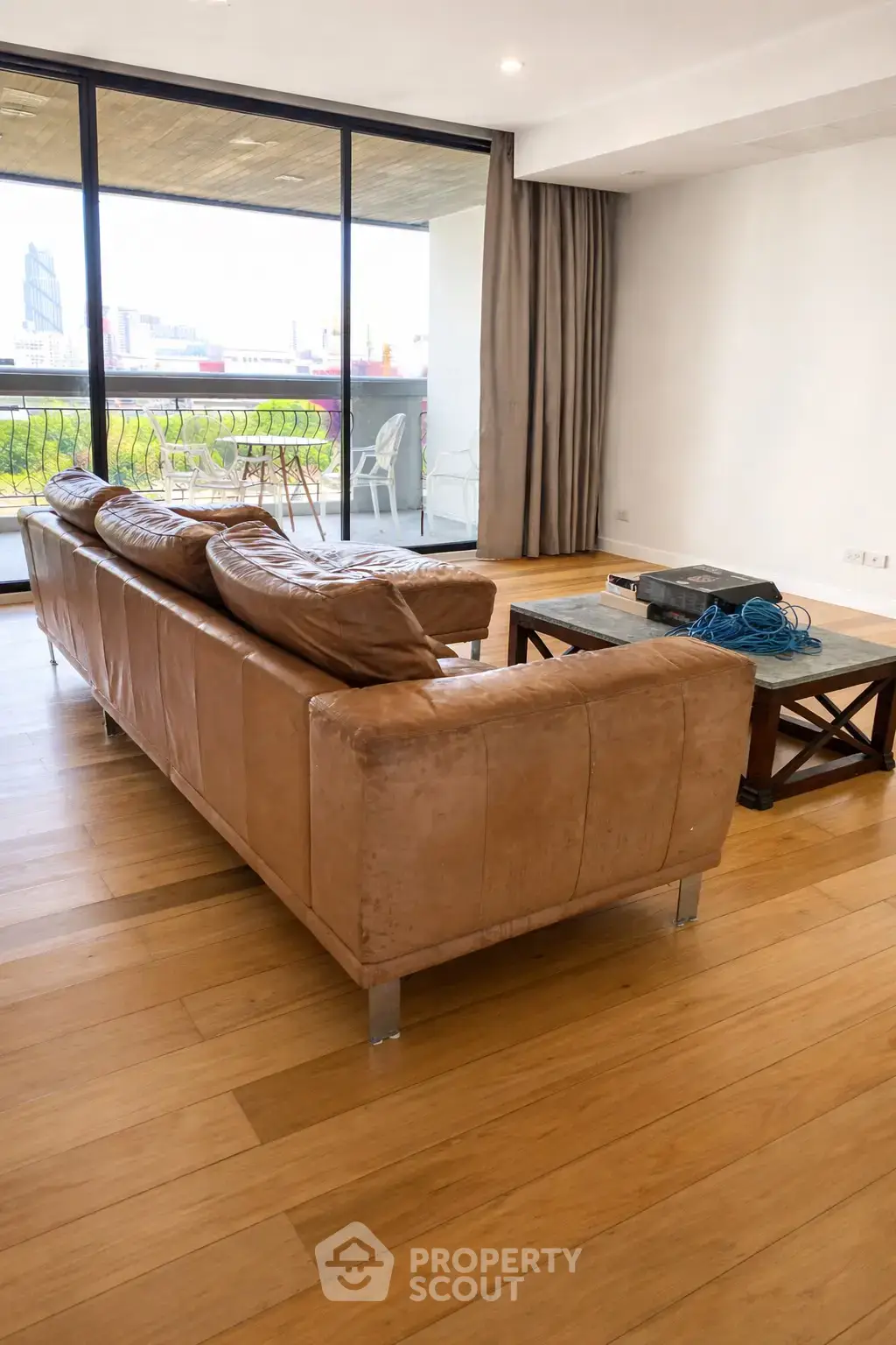 Spacious living room with leather sofa and large windows opening to a balcony with city views.