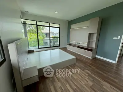 Spacious bedroom with large windows and modern built-in furniture, offering a serene view of greenery.