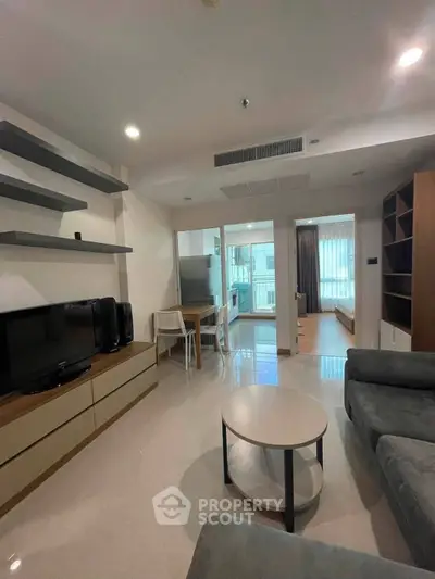 Modern living room with sleek furniture and open layout leading to kitchen and bedroom.