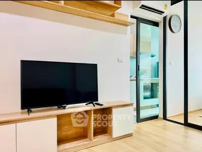 Modern living room with sleek TV setup and open kitchen view, showcasing contemporary design and functionality.