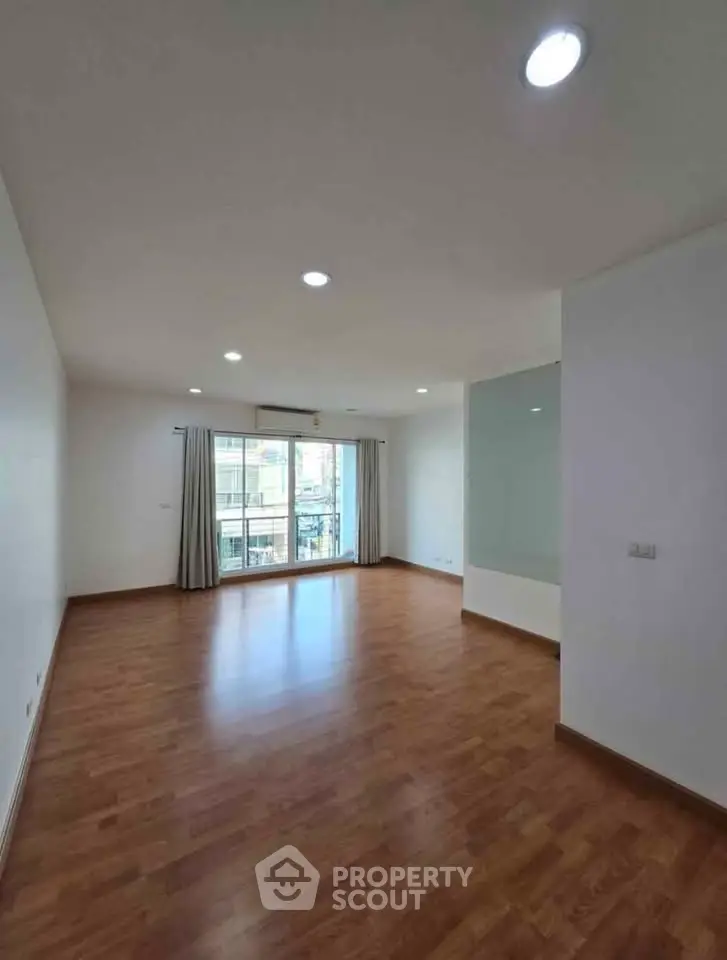 Spacious empty living room with wooden flooring and large window in modern apartment.