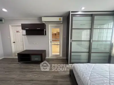 Modern bedroom with sleek wardrobe and air conditioning, featuring a glimpse into a stylish kitchen.
