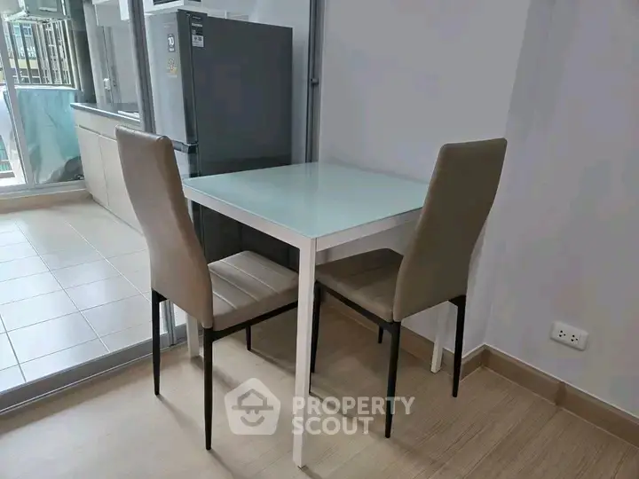 Modern dining area with glass table and two chairs in a bright apartment setting.