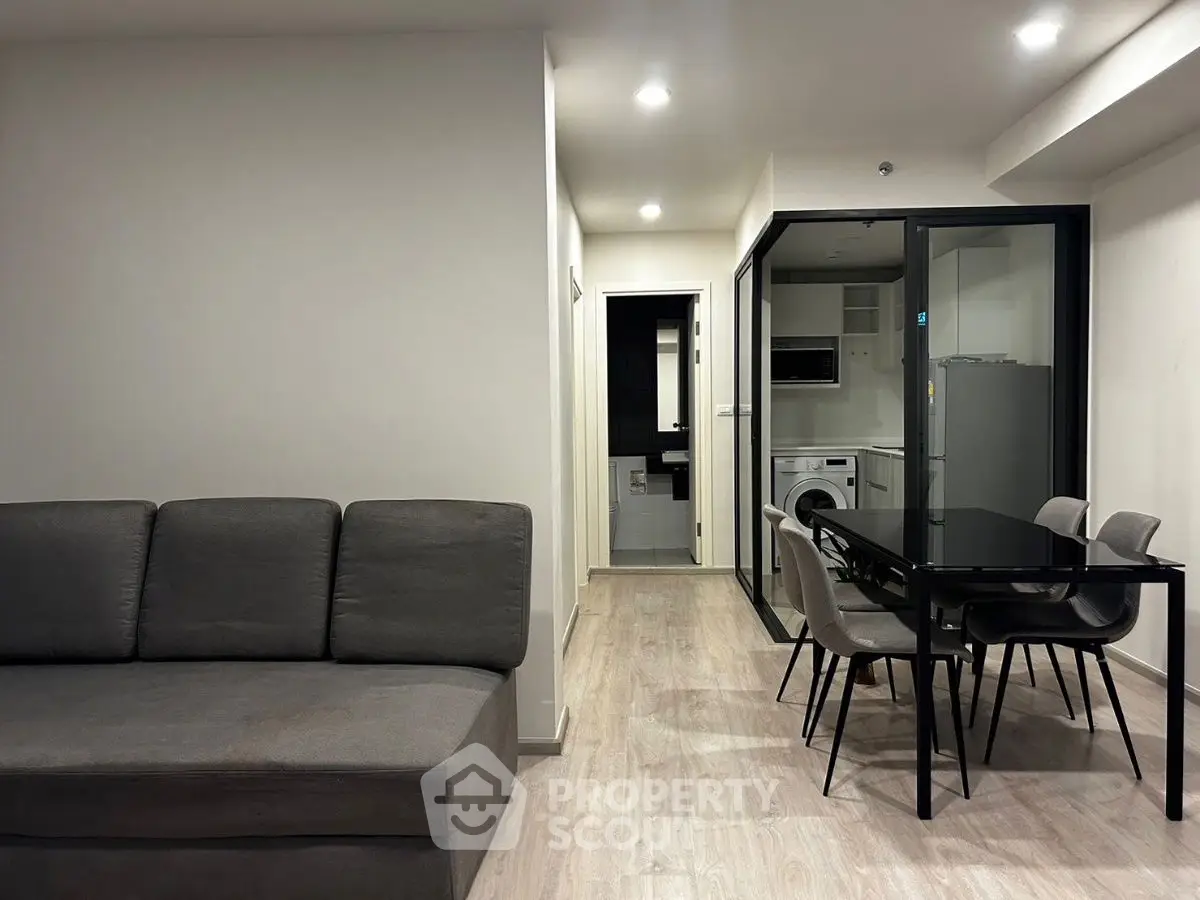 Modern living room with open kitchen and dining area, featuring sleek furniture and contemporary design.