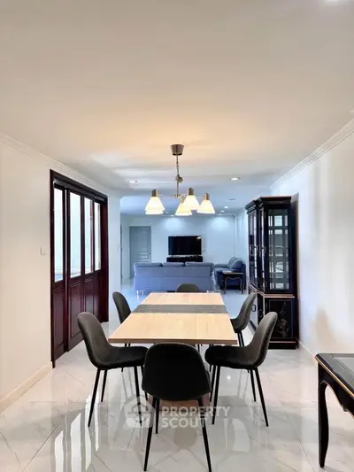 Elegant dining area with modern lighting and spacious living room view.
