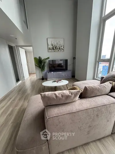 Spacious modern living room with high ceilings and large windows offering city views.