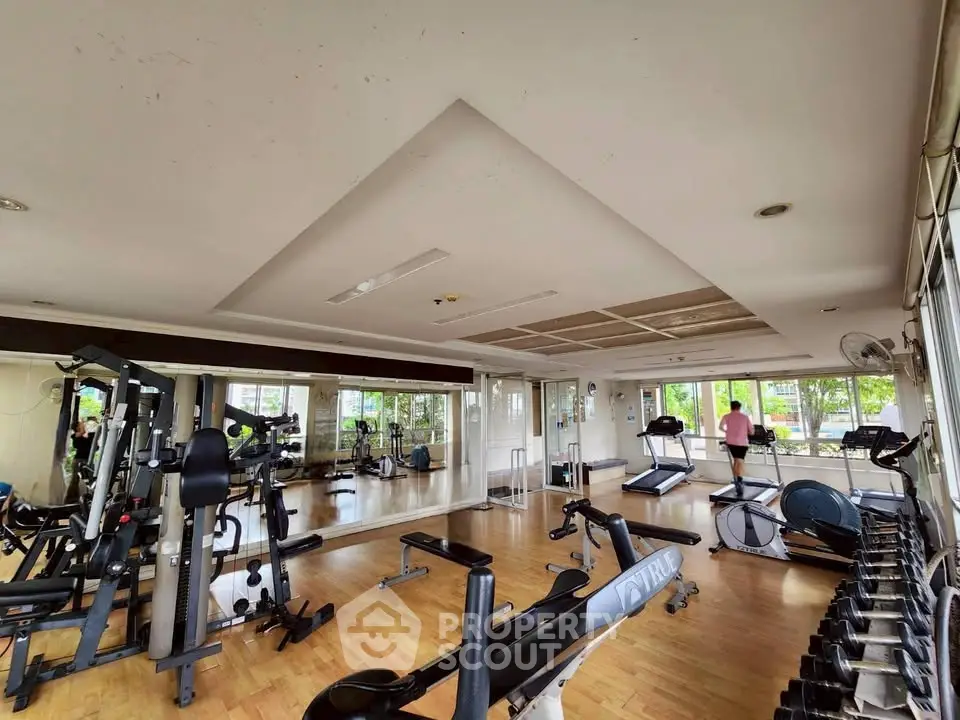 Spacious gym with modern equipment and large windows offering a bright workout environment.