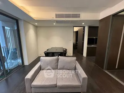 Modern living room with sleek furniture and dining area, featuring dark wood flooring and large windows.