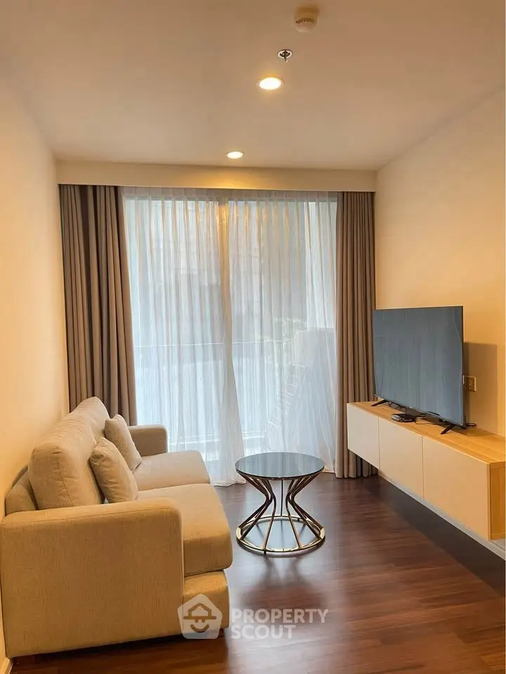Modern living room with cozy sofa, stylish table, and large TV, featuring floor-to-ceiling windows and elegant curtains.