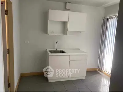Minimalist kitchen with white cabinetry and sink, natural light through vertical blinds.
