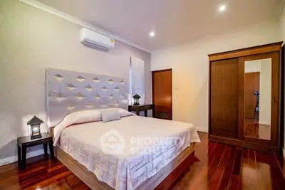 Elegant bedroom with wooden flooring and stylish furniture, featuring a plush bed and mirrored wardrobe.