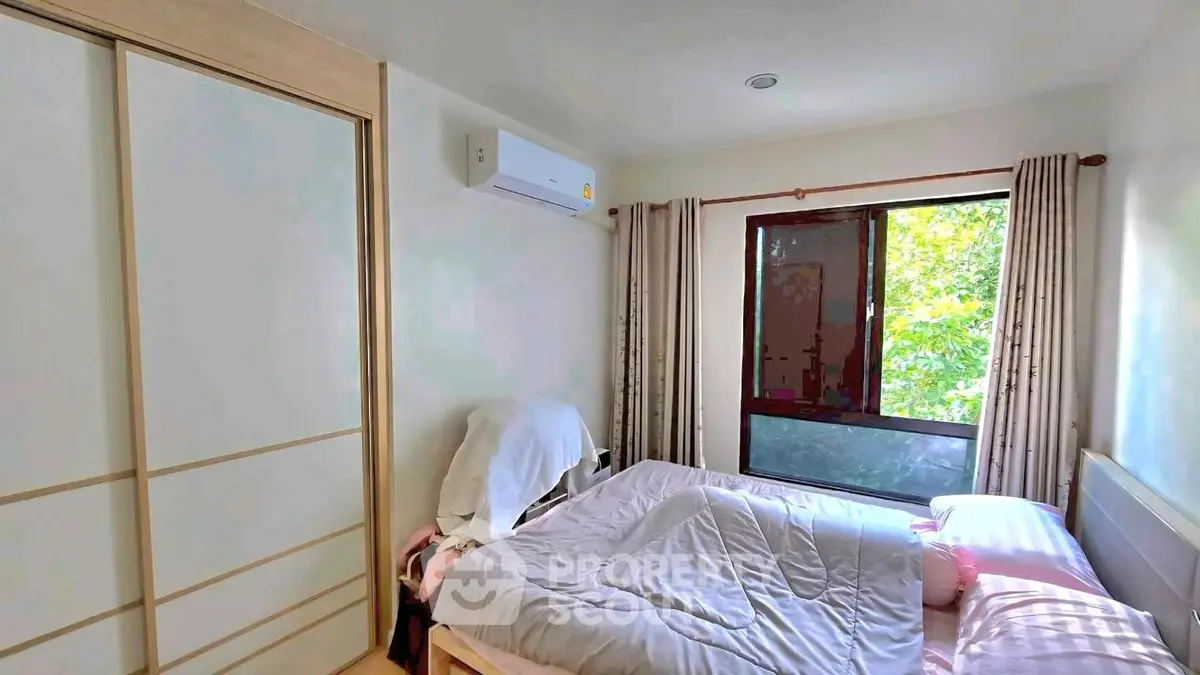 Cozy bedroom with large window and air conditioning, featuring a comfortable bed and ample natural light.