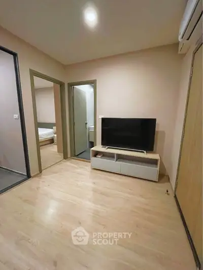 Modern apartment interior with wooden flooring, TV setup, and visible bedroom entrance.