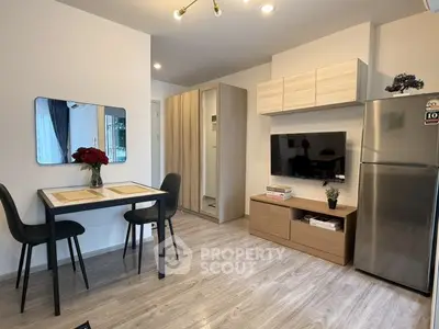 Modern living room with dining area, sleek furniture, and stainless steel fridge in a cozy apartment.