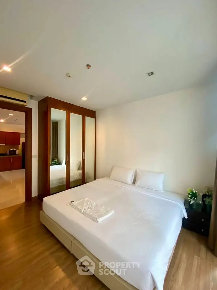 Spacious bedroom with elegant wooden flooring and mirrored wardrobe in modern apartment.
