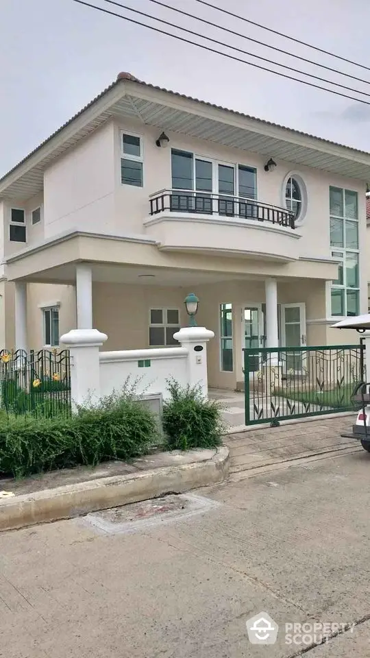 Modern two-story house with balcony and gated entrance in a suburban neighborhood.