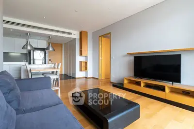 Modern living room with sleek furniture and open kitchen layout, featuring a large TV and stylish decor.