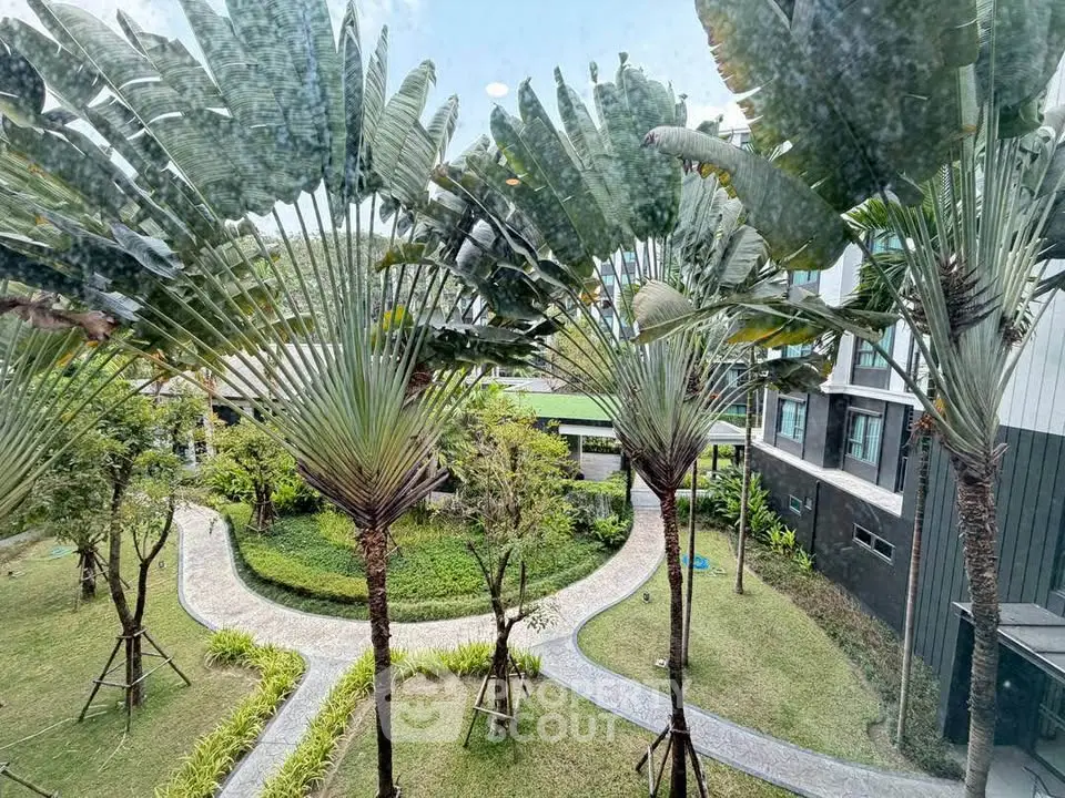 Lush garden view from modern apartment building with palm trees and winding pathways.