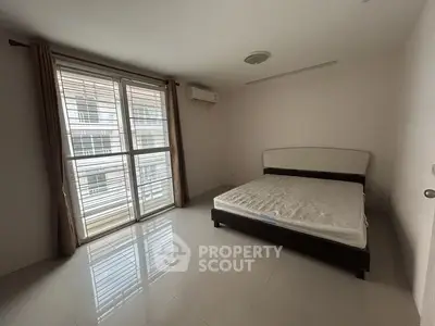 Spacious bedroom with large window and modern furnishings in a bright apartment.