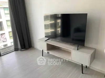 Modern living room with sleek TV stand and large flat-screen TV near window.