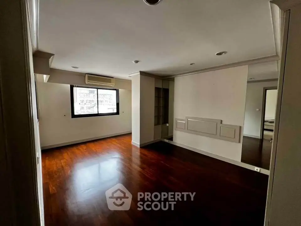Spacious empty room with wooden flooring and large window, ideal for customization.