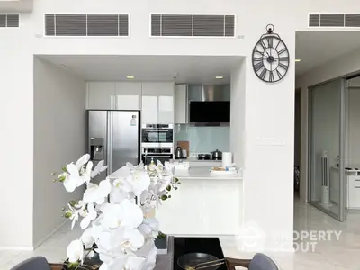 Modern kitchen with stainless steel appliances, white cabinetry, and a sleek breakfast bar, complemented by a spacious living area.