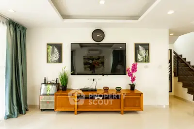 Spacious living room with modern decor, large TV, and elegant staircase in a bright home.